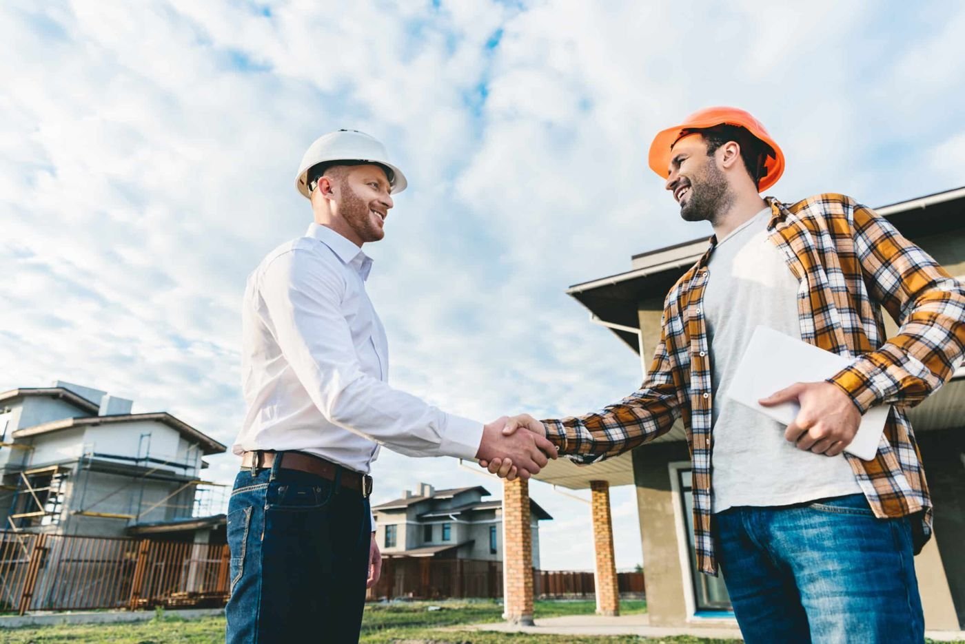 smiling architects shaking hands in front of construction site