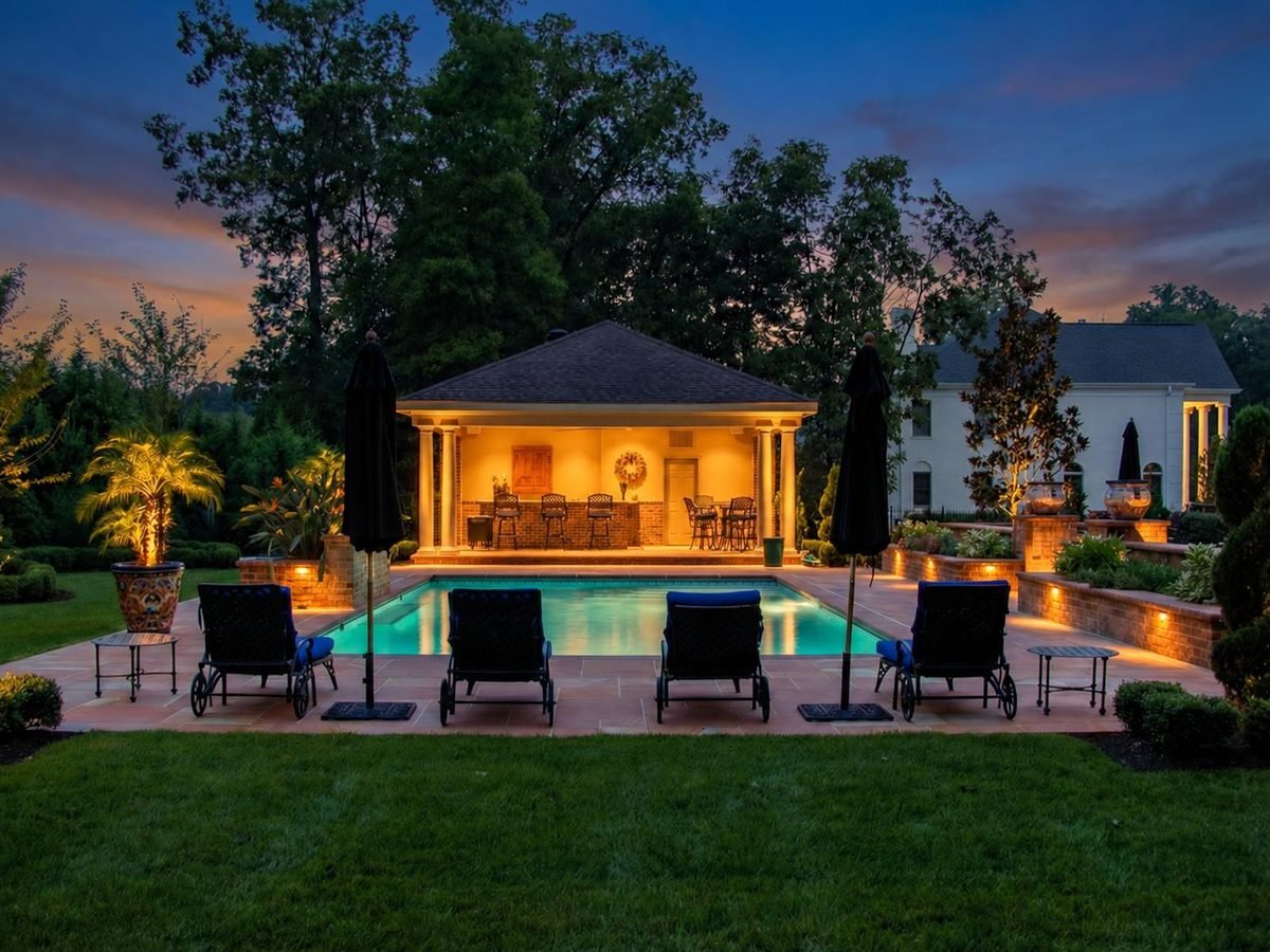 Pool house bar and outdoor lounge seating beside a lit pool at sunset